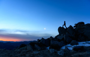 Person standing on rock overlooking blue mountain skyline