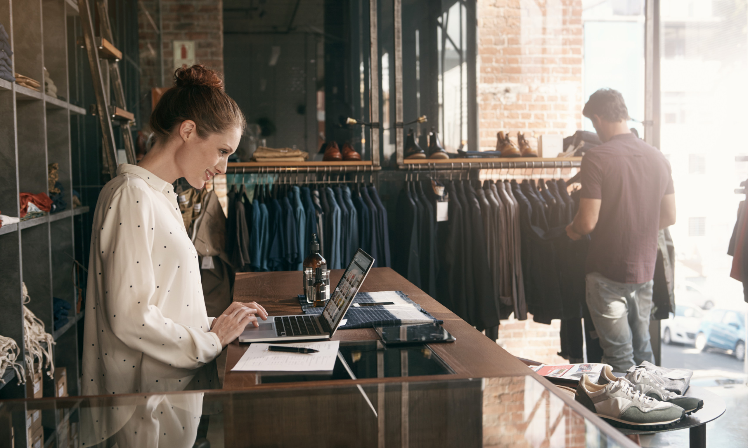 Young woman on a Macbook at the counter of her clothing boutique